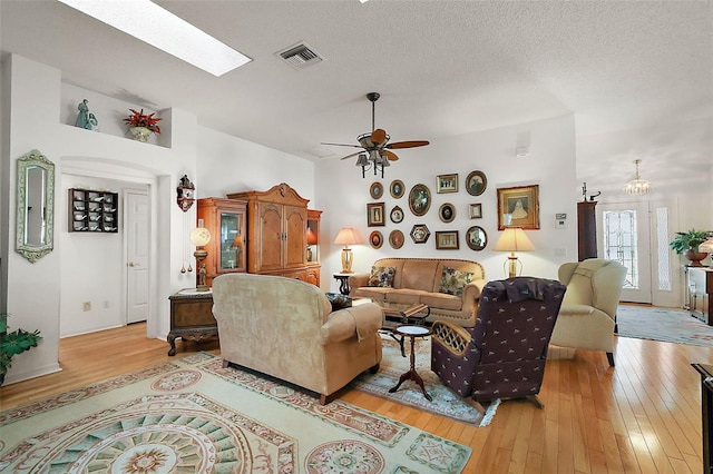 living room with a textured ceiling, a skylight, visible vents, a ceiling fan, and light wood-type flooring