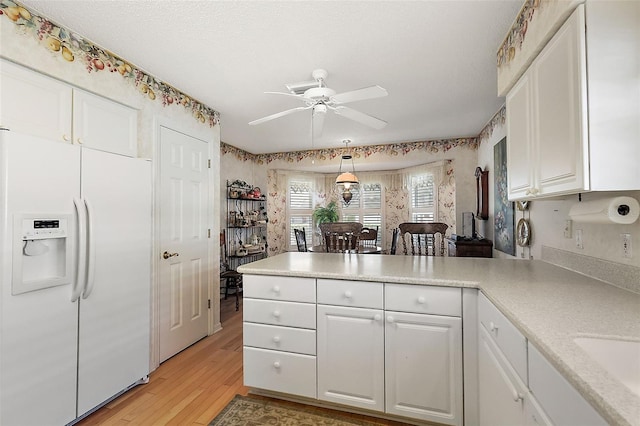 kitchen featuring light countertops, white refrigerator with ice dispenser, white cabinets, and a peninsula