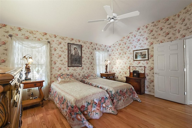 bedroom featuring wallpapered walls, baseboards, light wood-style flooring, ceiling fan, and vaulted ceiling