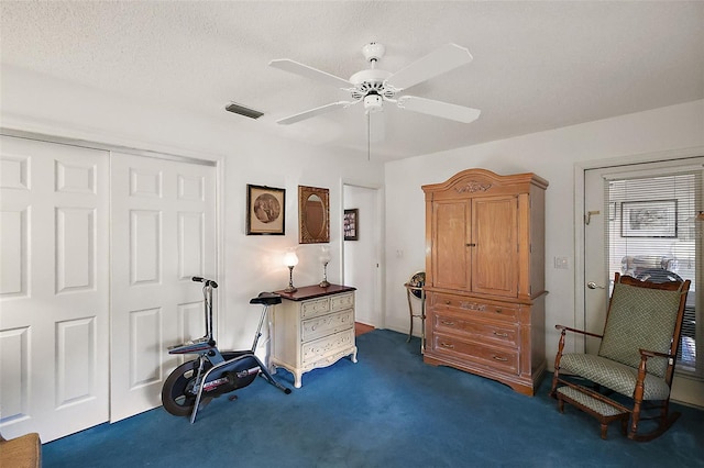 interior space featuring dark colored carpet, visible vents, ceiling fan, and a textured ceiling