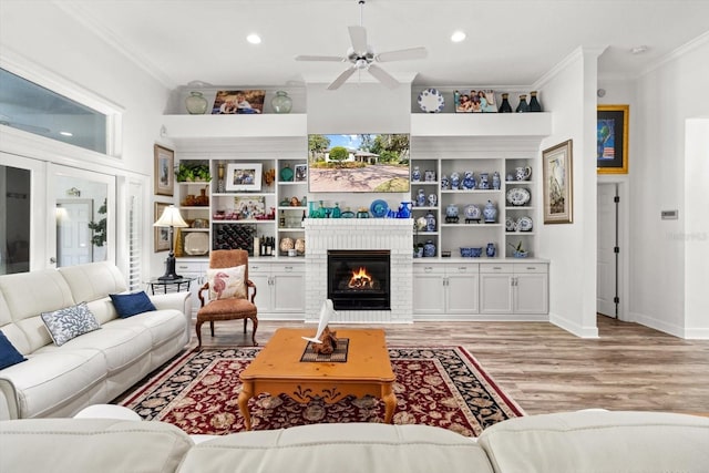 living room with light wood-type flooring, ceiling fan, ornamental molding, and a fireplace