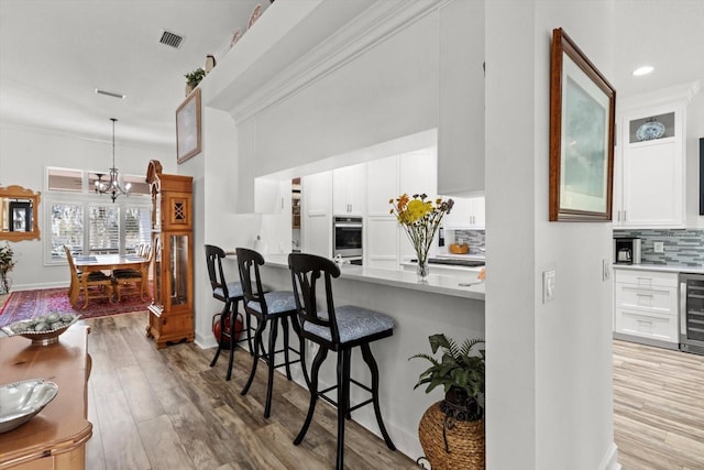 kitchen featuring white cabinetry, hanging light fixtures, light hardwood / wood-style floors, backsplash, and beverage cooler