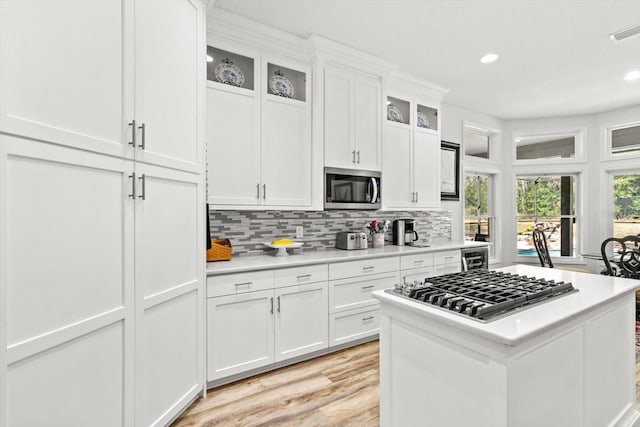 kitchen with appliances with stainless steel finishes, backsplash, beverage cooler, light hardwood / wood-style floors, and white cabinets