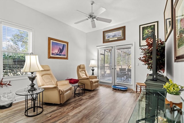 sitting room featuring ceiling fan, a wood stove, wood-type flooring, and a wealth of natural light