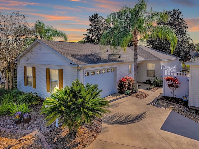 view of front facade featuring an attached garage, a shingled roof, fence, and concrete driveway