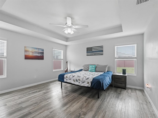 bedroom with a raised ceiling, visible vents, baseboards, and wood finished floors