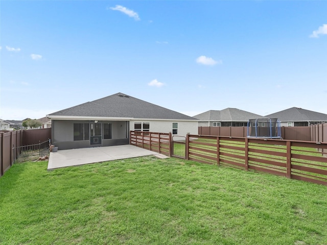 back of house featuring a patio, a trampoline, a fenced backyard, and a lawn