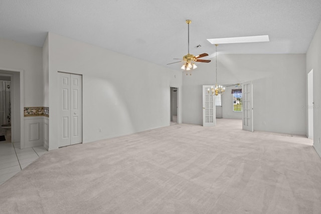 unfurnished living room with light carpet, a skylight, a textured ceiling, french doors, and ceiling fan with notable chandelier