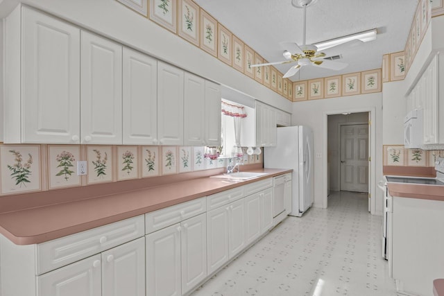 kitchen with white appliances, white cabinetry, a sink, and light floors