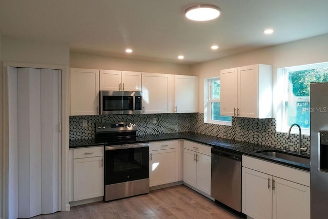 kitchen with light wood-type flooring, sink, backsplash, appliances with stainless steel finishes, and white cabinets