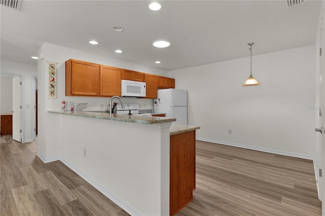 620 Vagabond St, The Villages, FL 32163 - kitchen with white appliances, light stone counters, brown cabinets, a peninsula, and hanging light fixtures