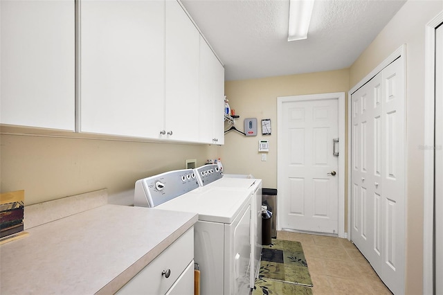 washroom with cabinet space, washer and clothes dryer, a textured ceiling, and light tile patterned flooring