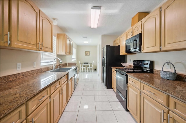 kitchen with light tile patterned floors, sink, dark stone counters, and black appliances