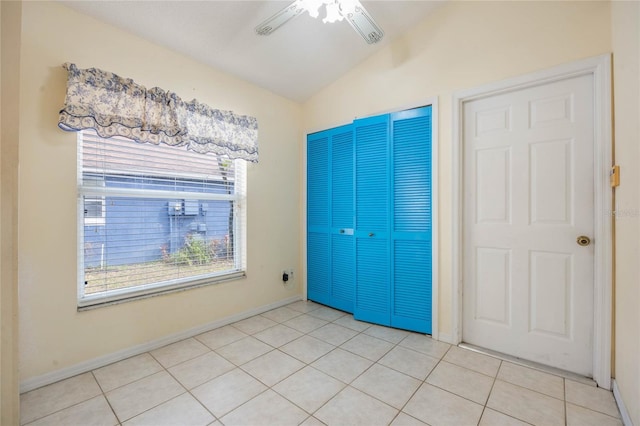 unfurnished bedroom featuring lofted ceiling, ceiling fan, light tile patterned flooring, baseboards, and a closet