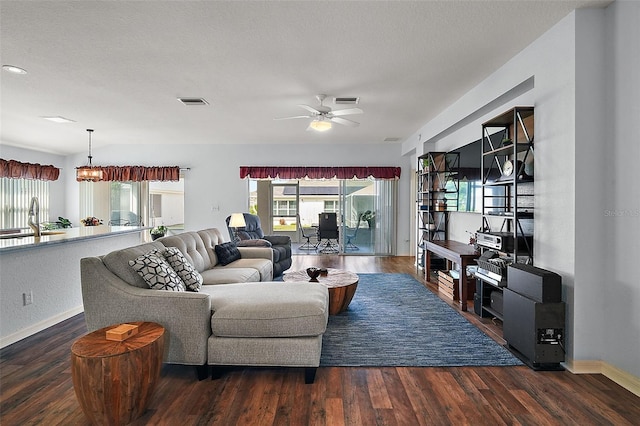 living room featuring dark wood-type flooring, visible vents, baseboards, and a ceiling fan