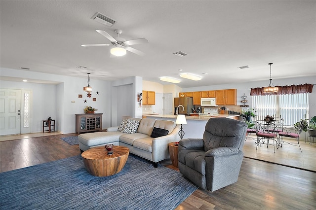 living room featuring ceiling fan with notable chandelier, wood finished floors, and visible vents