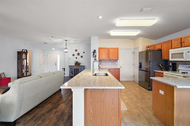 kitchen featuring white appliances, tasteful backsplash, an island with sink, open floor plan, and a sink