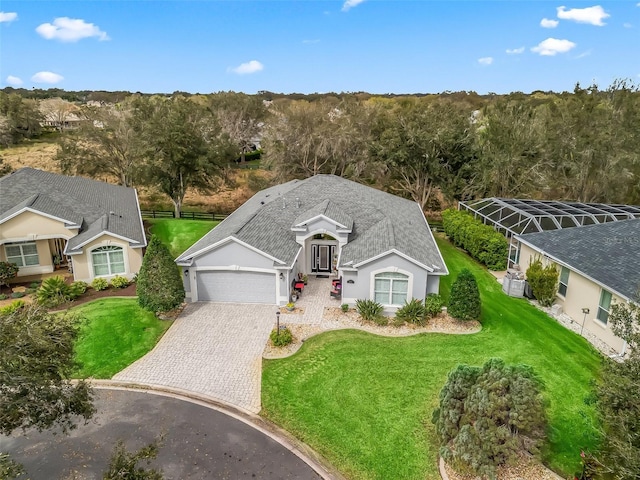 ranch-style house with a garage, glass enclosure, decorative driveway, and a front yard