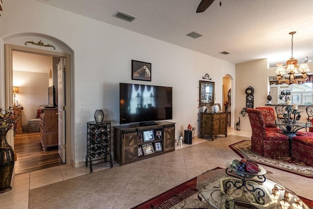 tiled living room featuring a textured ceiling and ceiling fan with notable chandelier