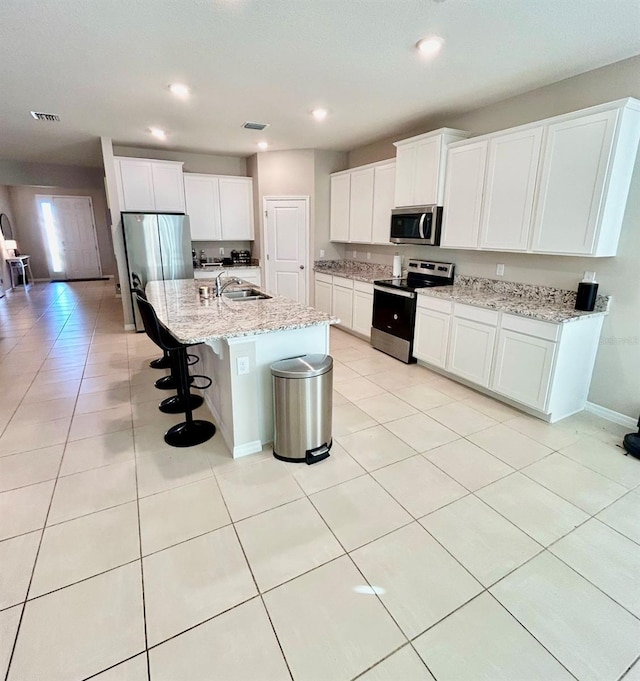 kitchen with light tile patterned floors, stainless steel appliances, visible vents, white cabinets, and a kitchen bar