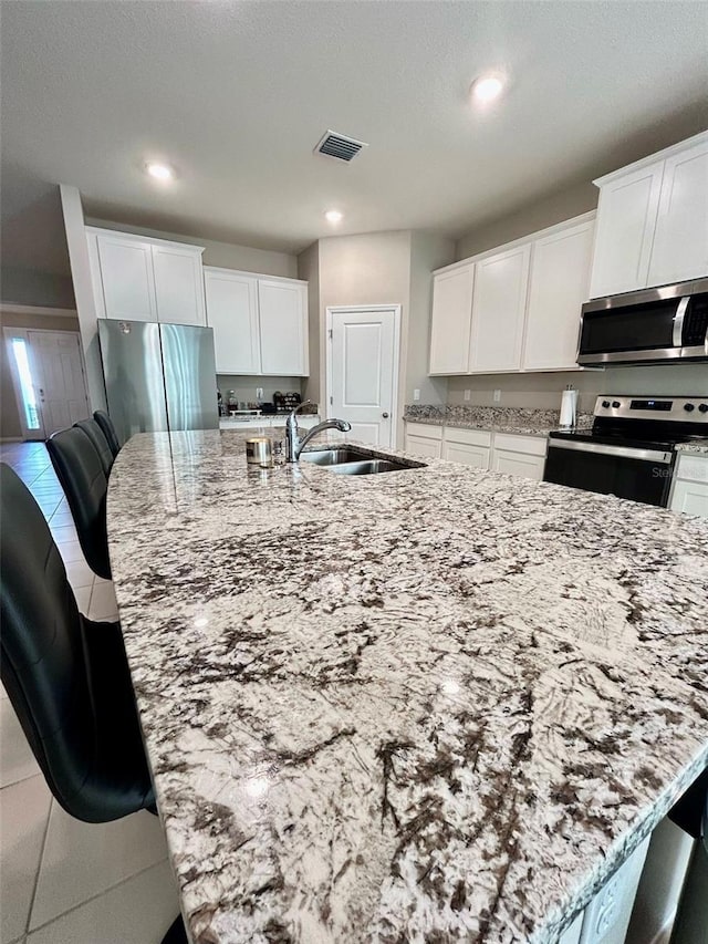 kitchen with stainless steel appliances, visible vents, a sink, and light stone counters