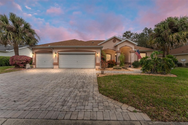 mediterranean / spanish home featuring an attached garage, a lawn, decorative driveway, and stucco siding