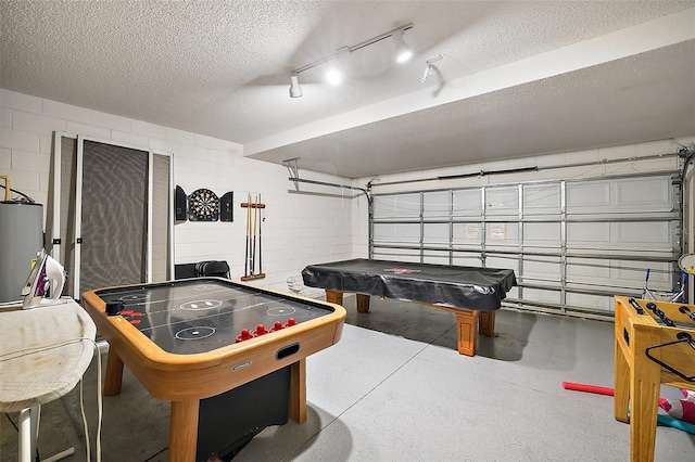 playroom with a textured ceiling, light speckled floor, a garage, water heater, and concrete block wall