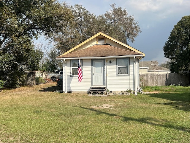 rear view of property featuring a shingled roof, entry steps, a yard, and fence