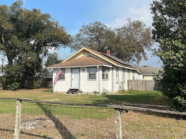 bungalow with entry steps, a chimney, fence, roof mounted solar panels, and a front yard