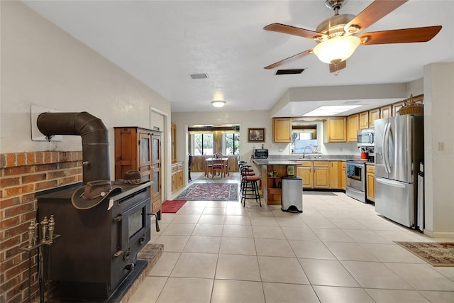 kitchen featuring a breakfast bar area, visible vents, appliances with stainless steel finishes, a wood stove, and light tile patterned flooring