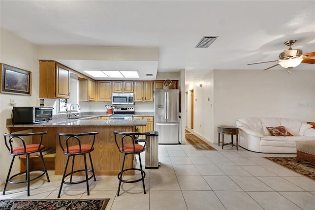 kitchen featuring stainless steel appliances, a peninsula, a sink, visible vents, and a kitchen bar