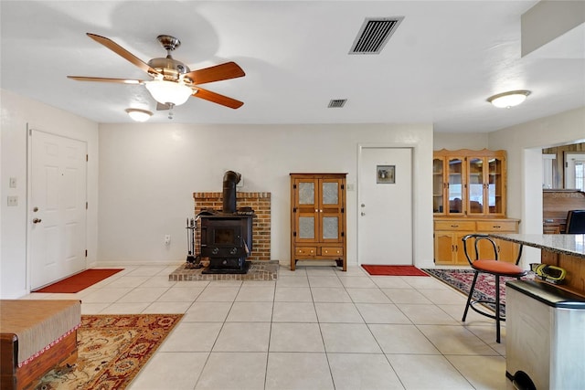 living area with ceiling fan, light tile patterned flooring, visible vents, baseboards, and a wood stove