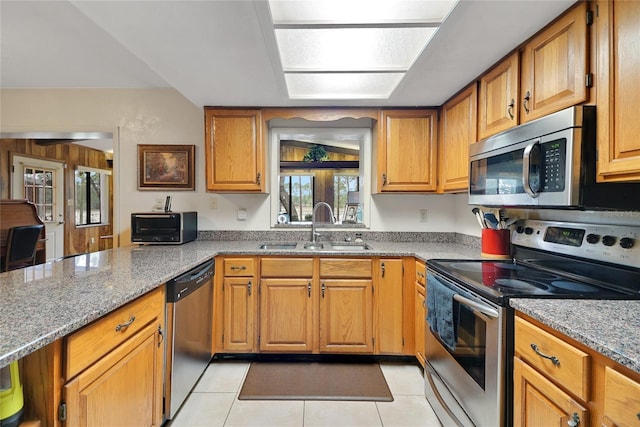 kitchen featuring brown cabinetry, appliances with stainless steel finishes, light stone counters, and a sink