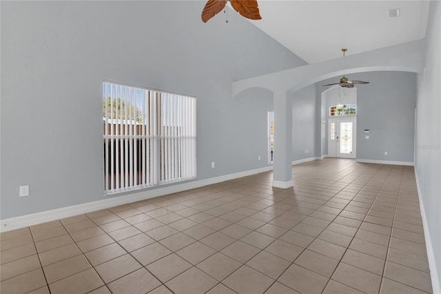 unfurnished room with ceiling fan, high vaulted ceiling, light tile patterned floors, arched walkways, and baseboards