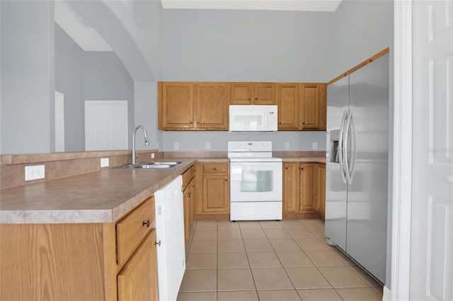 kitchen with light tile patterned floors, white appliances, a sink, a towering ceiling, and light countertops