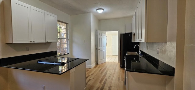 kitchen with a sink, white cabinetry, light wood-type flooring, black appliances, and dark countertops