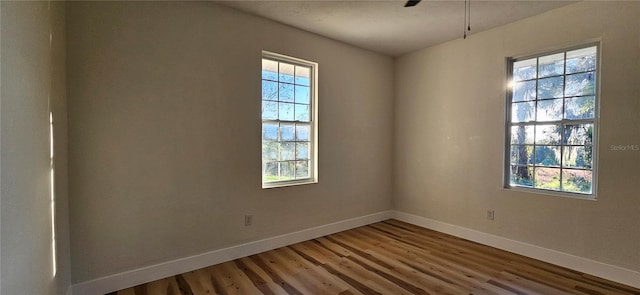 unfurnished room with plenty of natural light, wood finished floors, and baseboards