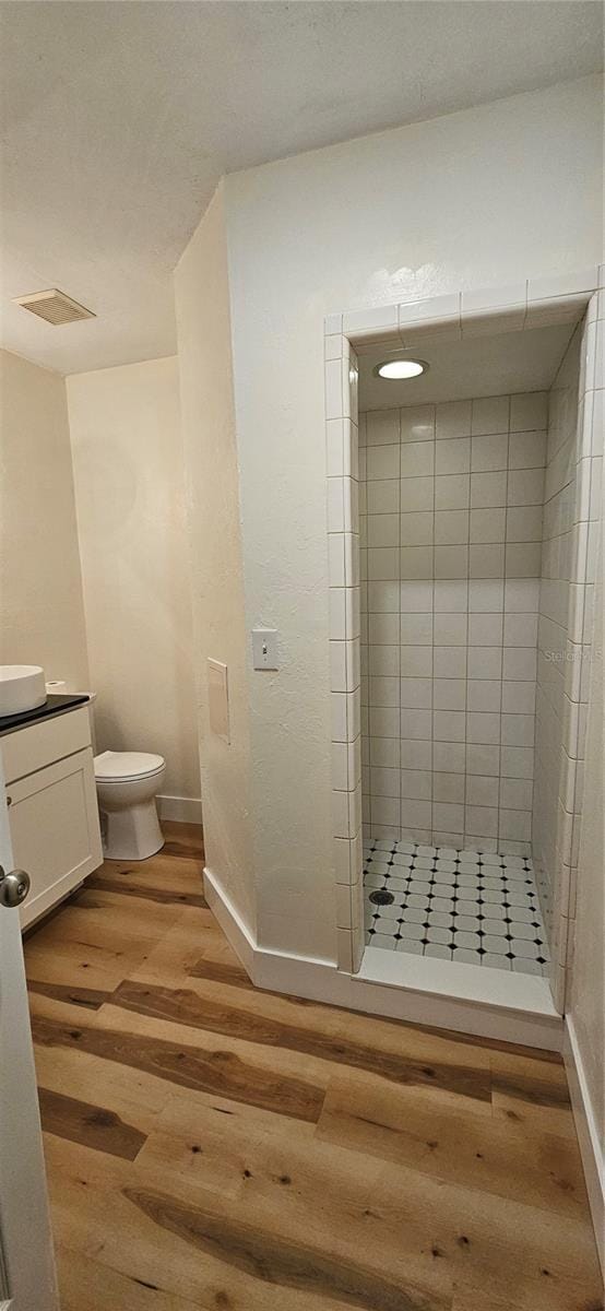 bathroom featuring visible vents, toilet, vanity, wood finished floors, and tiled shower