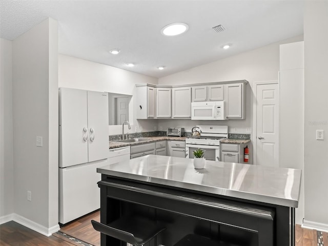 kitchen featuring white appliances, visible vents, a kitchen island, dark wood-type flooring, and a sink