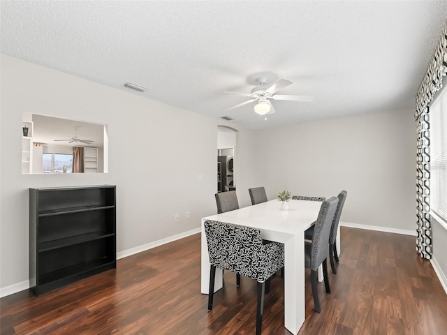 dining space featuring dark wood-style flooring, visible vents, ceiling fan, a textured ceiling, and baseboards