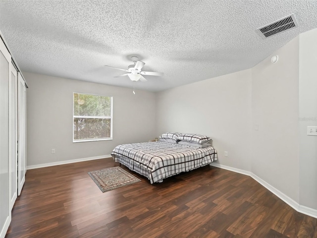 bedroom featuring visible vents, dark wood finished floors, baseboards, ceiling fan, and a textured ceiling