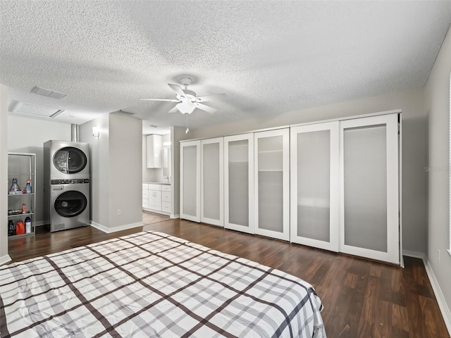 unfurnished bedroom featuring dark wood-style floors, a textured ceiling, baseboards, and stacked washer / drying machine