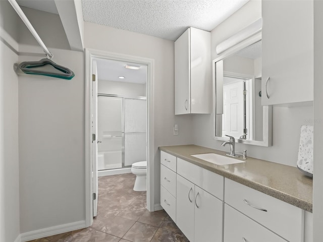 full bath with toilet, a stall shower, vanity, a textured ceiling, and baseboards