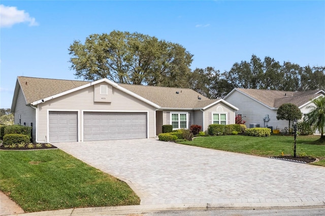 ranch-style house featuring an attached garage, decorative driveway, and a front yard