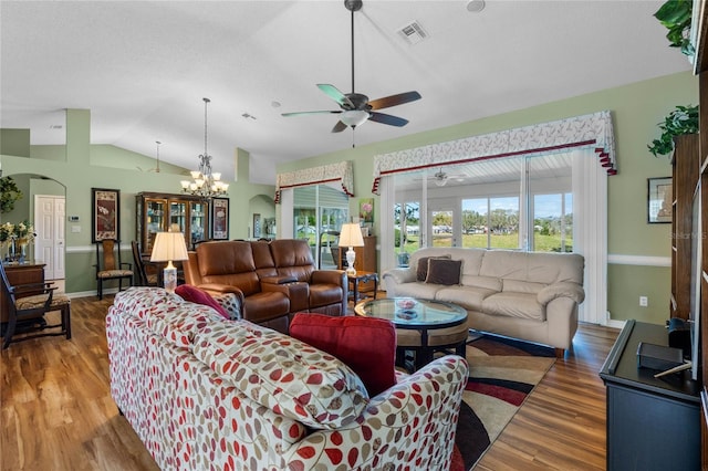 living room with lofted ceiling, arched walkways, ceiling fan with notable chandelier, wood finished floors, and visible vents