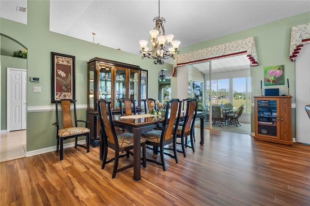 dining space with lofted ceiling, wood finished floors, visible vents, and a notable chandelier