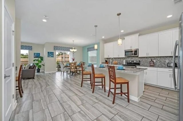 kitchen featuring a breakfast bar area, white cabinets, appliances with stainless steel finishes, decorative light fixtures, and backsplash