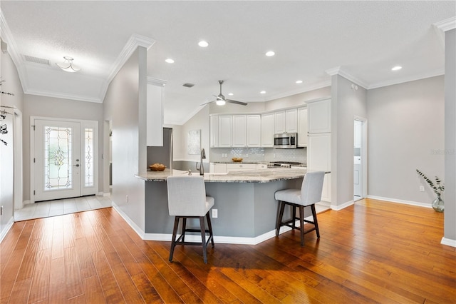 kitchen with a breakfast bar area, light stone countertops, white cabinetry, decorative backsplash, and stainless steel microwave