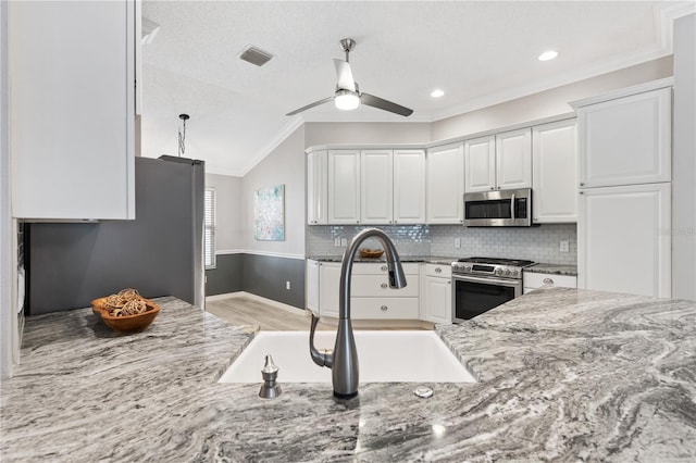 kitchen with light stone counters, stainless steel appliances, a sink, white cabinets, and vaulted ceiling