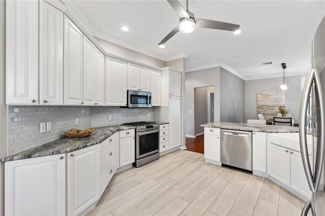 kitchen featuring stainless steel appliances, white cabinets, hanging light fixtures, and dark stone countertops